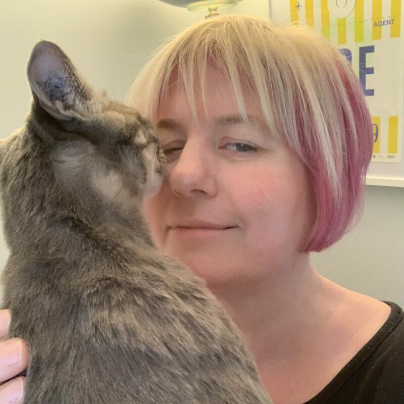 Lady with pink hair being bumped in the face by a grey tabby cat